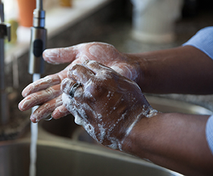 Closeup of hands in sink with running water. Hands are covered with soap suds.